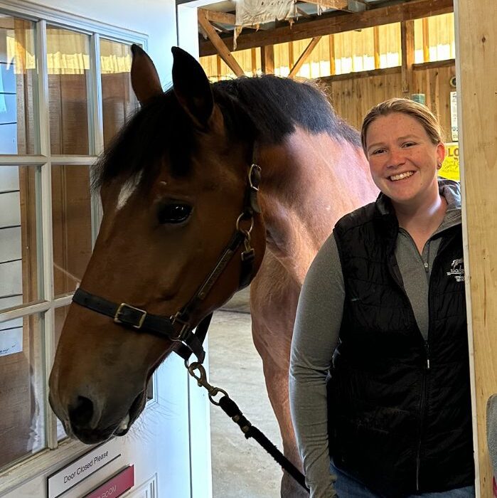 Hannah Jannell standing next to a horse in the barn